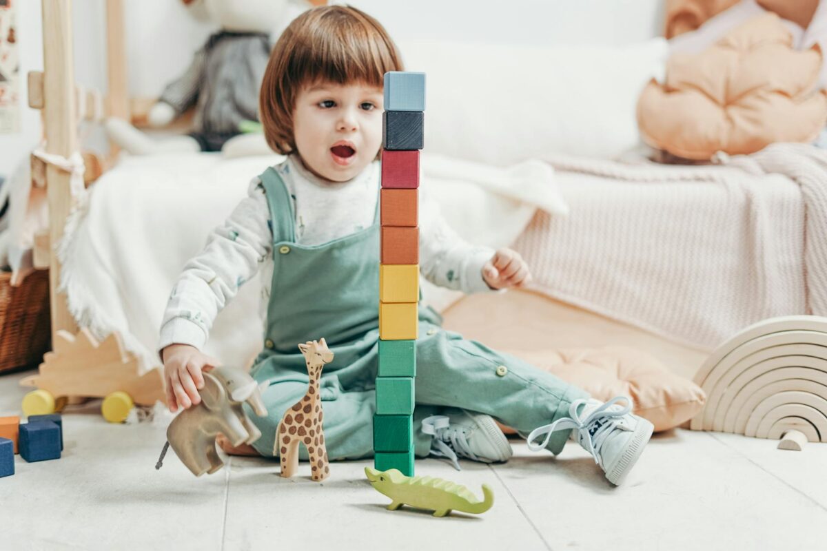 Toddler stacking colourful wooden blocks beside a toy giraffe